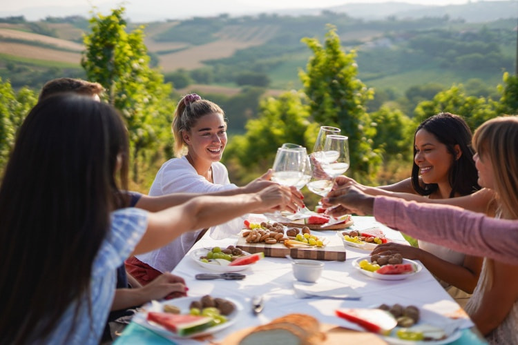 a group of women toast with glasses of wine outside at a vineyard